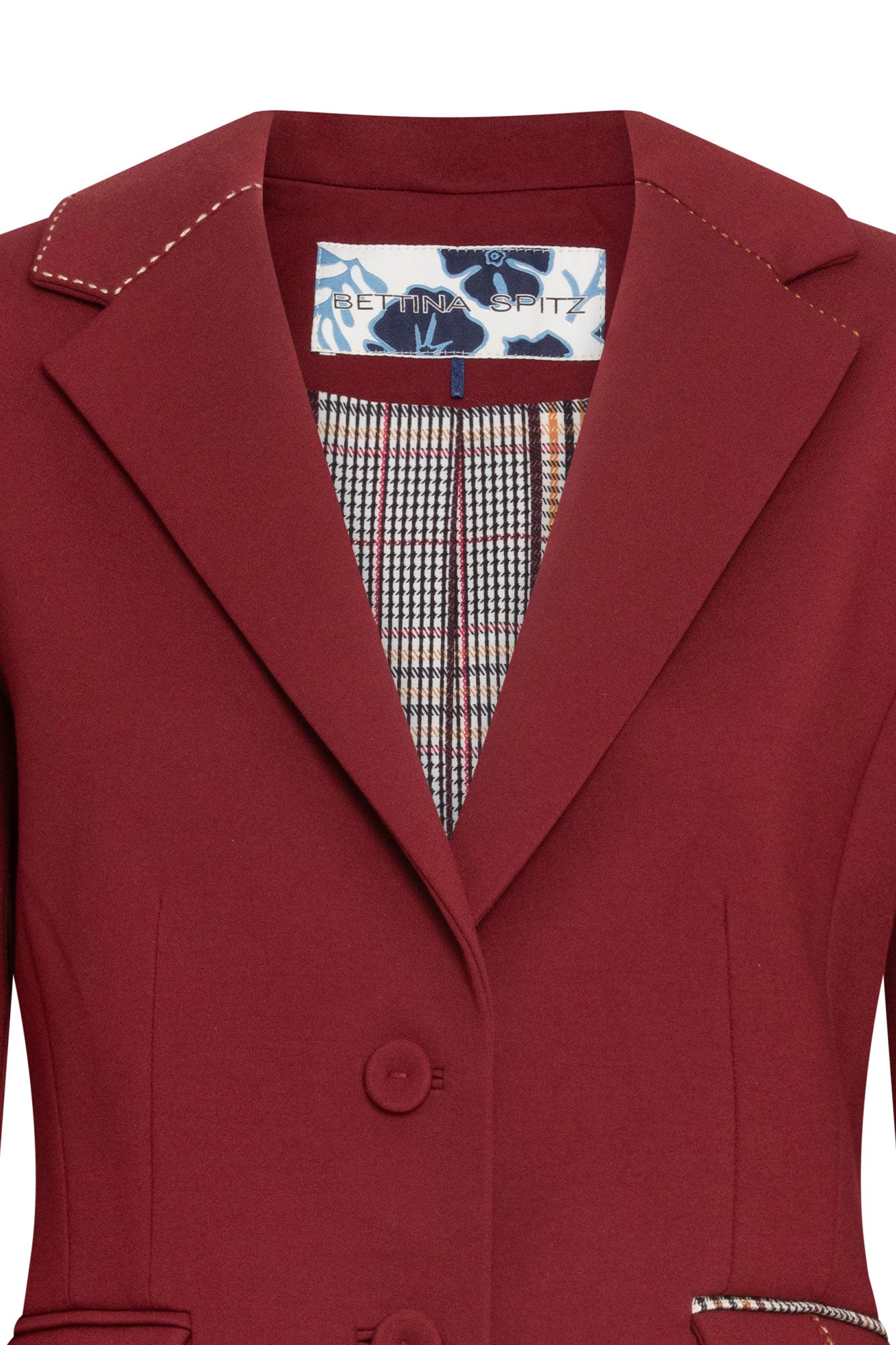 Blazer Juan PP Argollas Vino — close-up of front lapel and interior showing notched lapel with cream hand topstitch, Prince of Wales check lining in cream, brown, and black visible inside lapel opening, Bettina Spitz woven label on floral-print ground at center back neckline, and two-button front closure