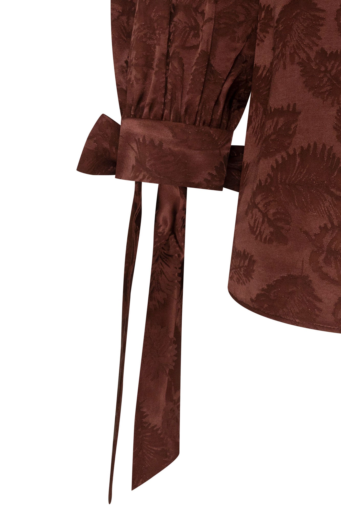 The Blusa Manga Puff Mono — close-up of structured wrist cuff band and long slim satin ribbon bow tie in chocolate brown showing flat bow and two long trailing ends against tonal floral jacquard fabric
