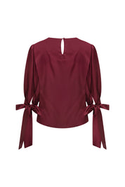 Back view of burgundy puff-sleeve blouse with buttoned keyhole closure and bow cuff ties