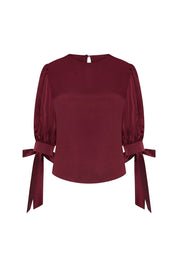 Front view of Bettina Spitz burgundy blouse with puff sleeves, round neckline and long bow cuff ties