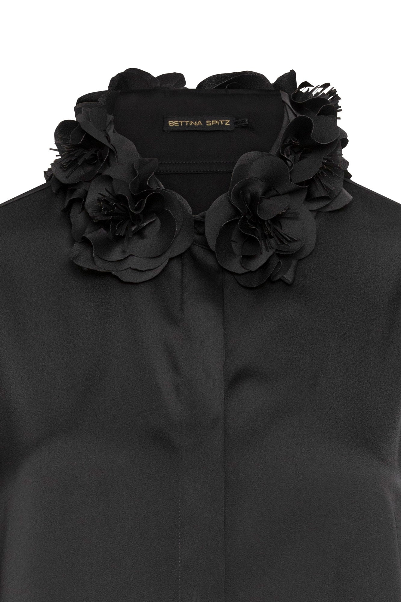The Verónica Black Satin Blouse — close-up of hand-crafted 3D black fabric roses with feathered petal edges at neckline and Bettina Spitz label