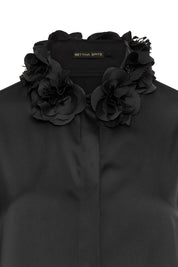 The Verónica Black Satin Blouse — close-up of hand-crafted 3D black fabric roses with feathered petal edges at neckline and Bettina Spitz label