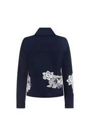 The Chaqueta Jean Flor Hilo Navy — full back view showing horizontal seam band at lower back and clusters of large-scale white botanical embroidery covering lower back panels against deep navy crepe, with single navy button at each cuff