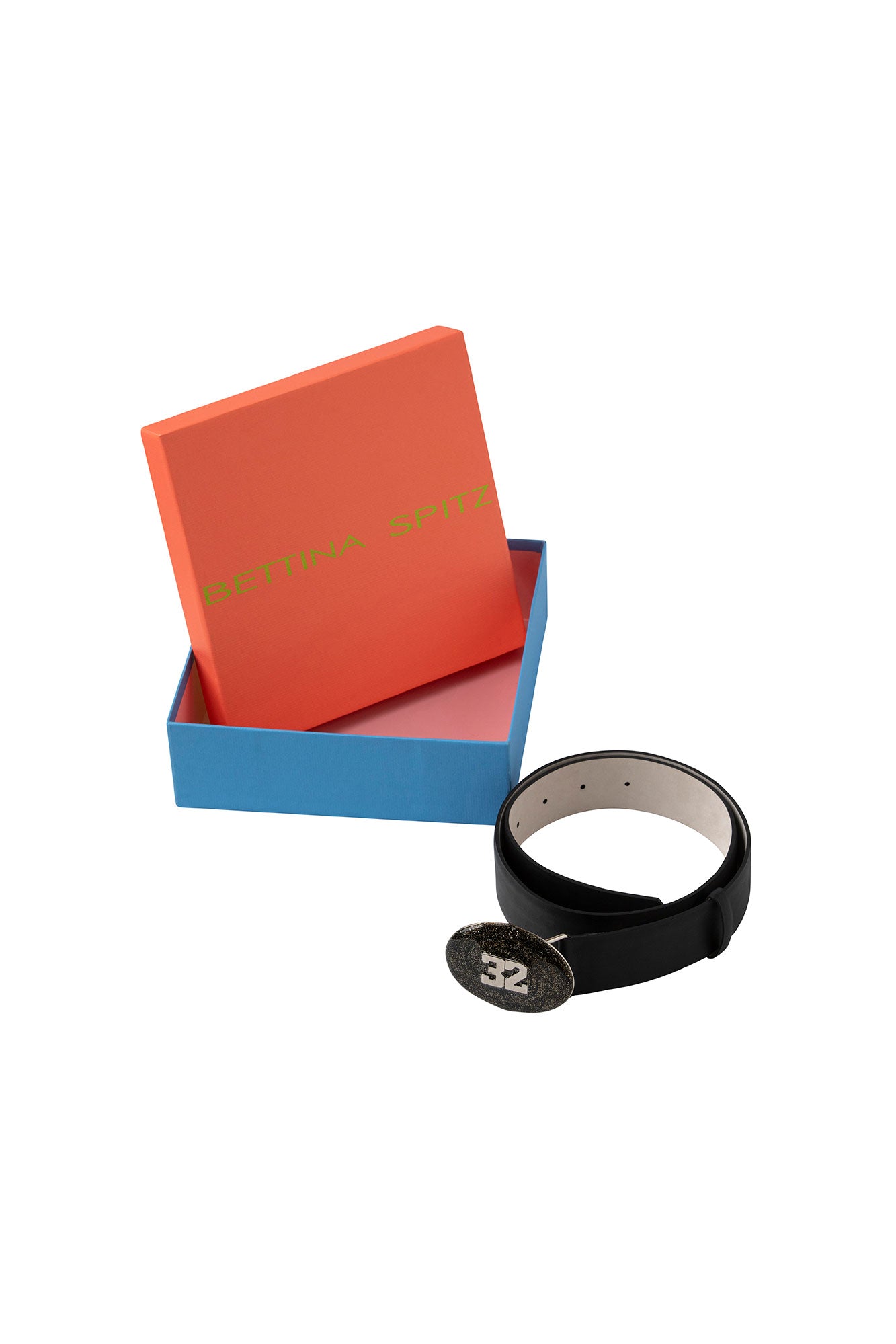 Rolled black belt with oval 32 buckle and adjustment holes beside a Bettina Spitz box