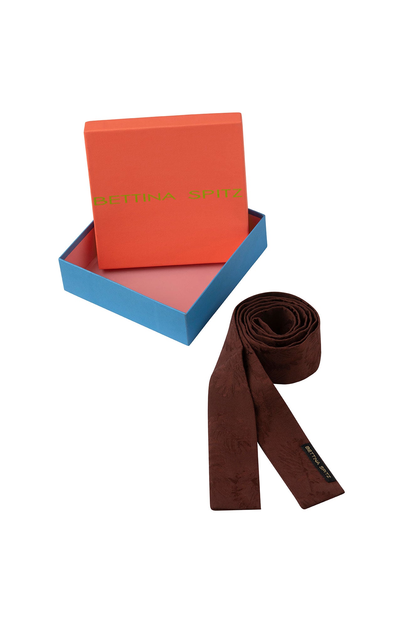 Rolled brown square-end tie with Bettina Spitz label beside an orange and blue branded box