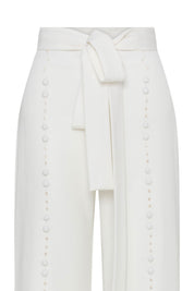Close-up of ivory trousers showing wide tie belt and vertical tonal button detailing