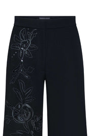 The Gaby Black Wide-Leg Trousers — close-up of hand-embroidered floral vine with tonal black thread, cutwork openwork petals, crystal accents and acrylic ring detail