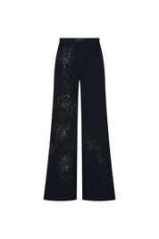 The Gaby Black Wide-Leg Trousers — full front view showing wide-leg flare silhouette and hand-embroidered botanical vine on left leg