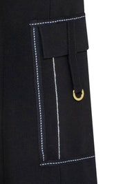 The Patch Campana — close-up of front thigh vertical panel pocket showing gold D-ring pull at lower edge and precise white contrast topstitching outline on black structured stretch fabric