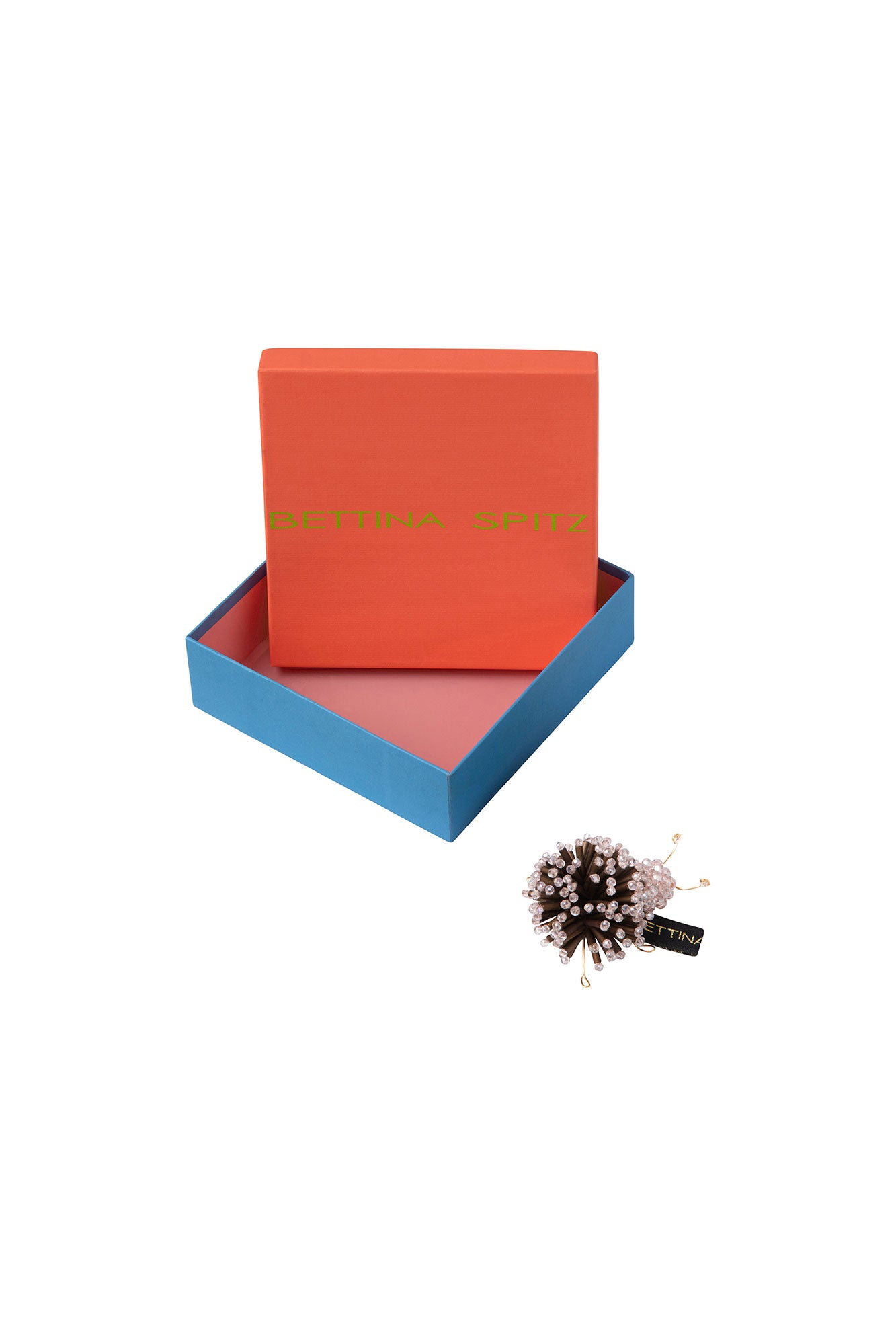 Brown and pale pink beaded Catarina brooch beside an open orange and blue Bettina Spitz box