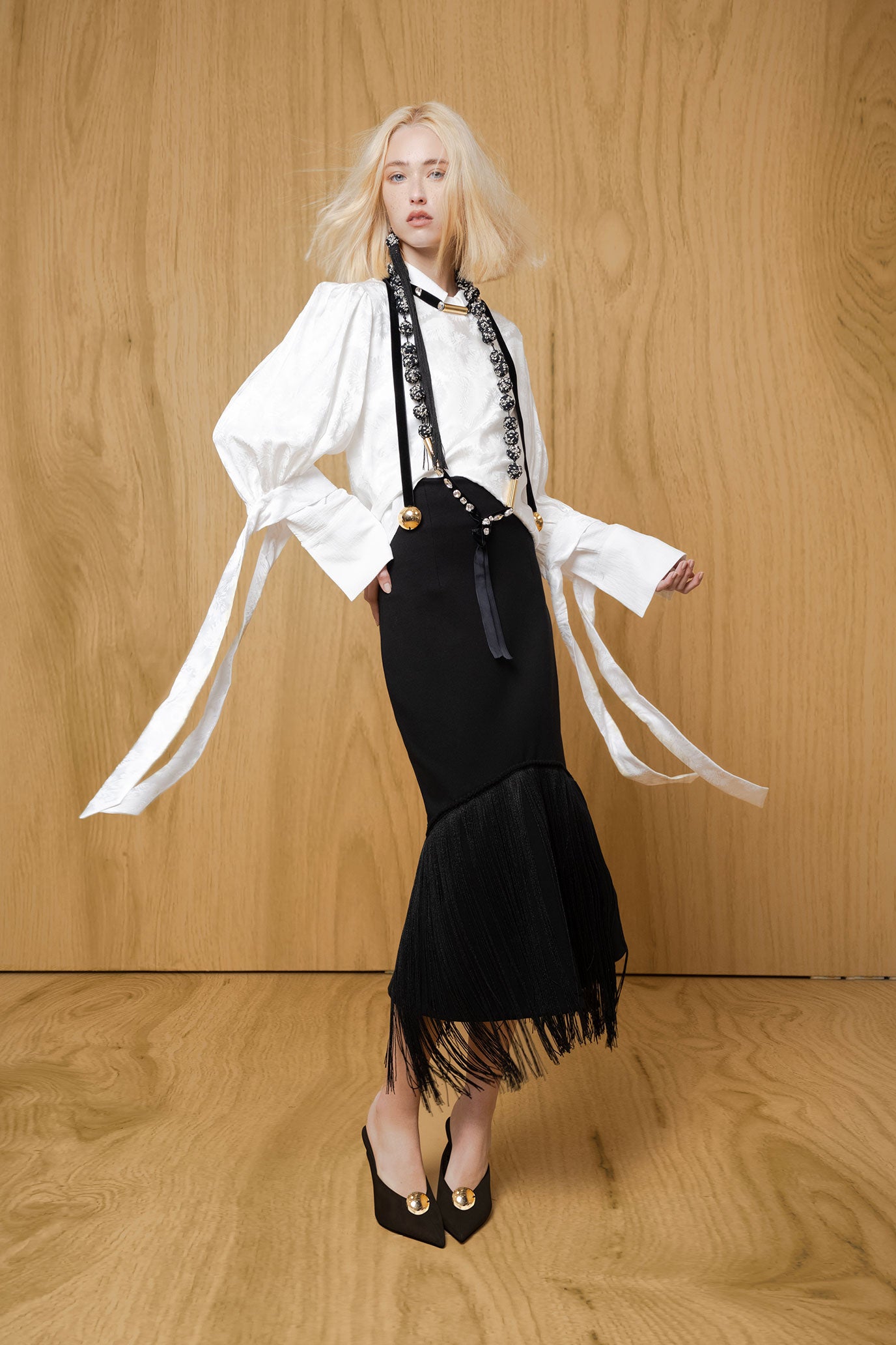 Closer model view of black midi skirt showing fitted silhouette, angled seam and long fringe at the flared hem